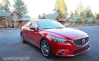 Picture of a cherry red Mazda 6 parked in front of cabins surrounded by trees.