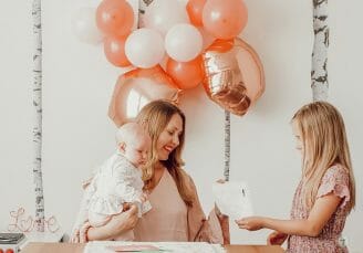 mom holding baby while older daughter hands her a drawing