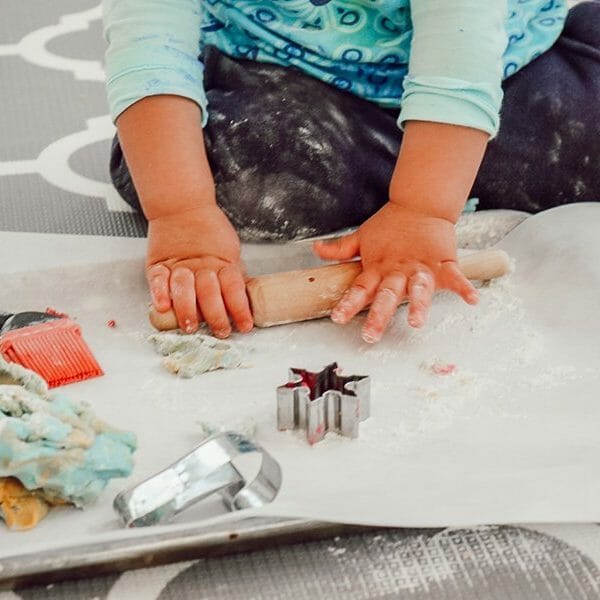 close up of toddler hands using rolling pin on playing dough in a sheet pan