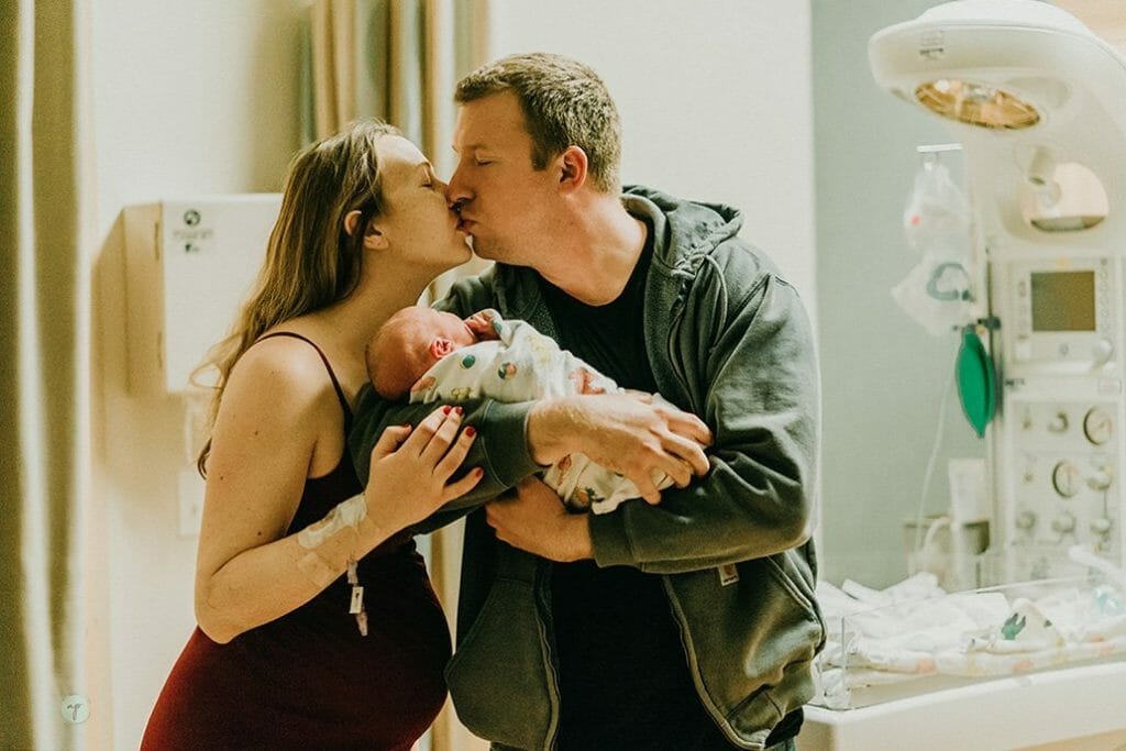 new parents hold baby after birth and kiss