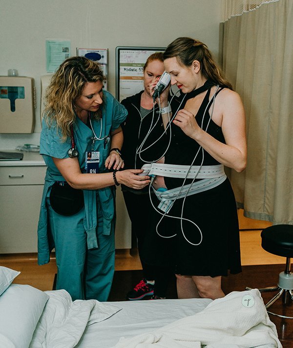 Nurse secures fetal heart monitor around birthing mother's belly so she can walk around