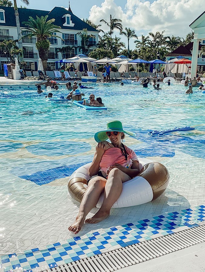 baby in ring sling asleep on mom who is sitting in a floaty in a pool