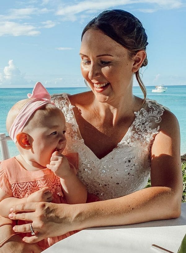 mom and calm teething baby feature image mom in wedding dress smiles down at baby in pink dress sitting on her lap and teething on her fingers