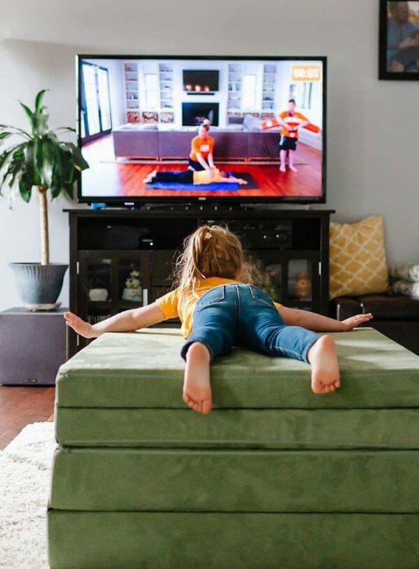 girl practices swimming exercises on green nugget sofa while watching YouTube