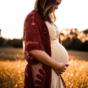 Pregnant woman holds belly while standing in wheat field