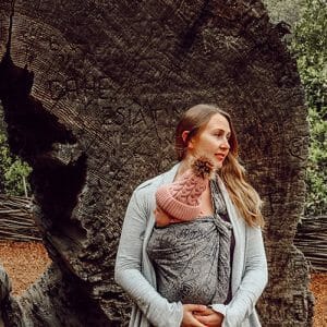babywearing mom holds baby near tree trunk