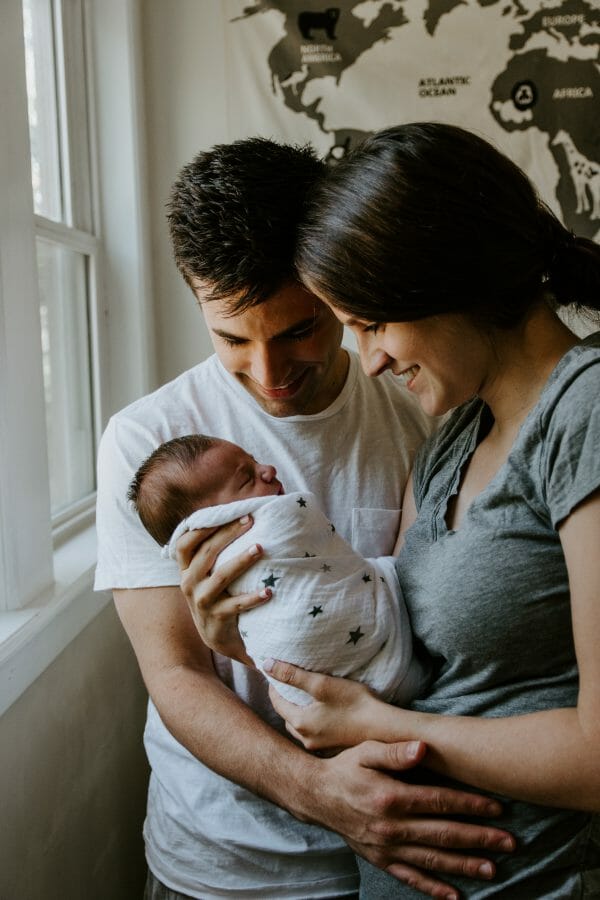 new postpartum parents hold swaddled newborn in their arms and smile