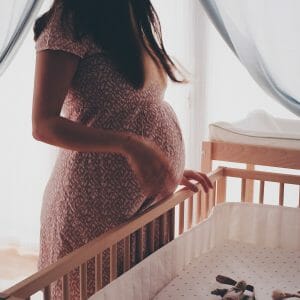 pregnant mom stands by empty crib