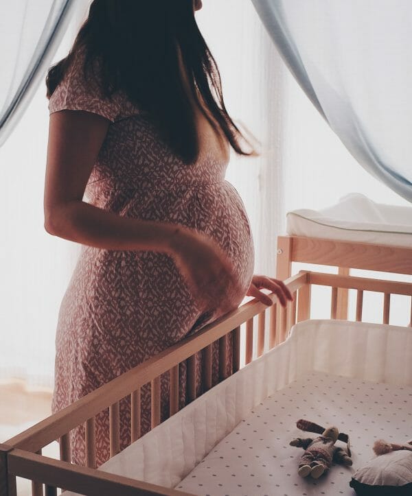 pregnant mom stands by empty crib